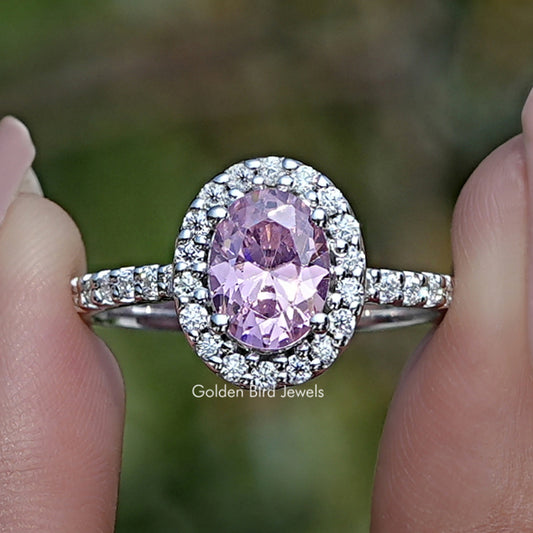 Oval pink gemstone halo ring with clear stone accents on a silver band