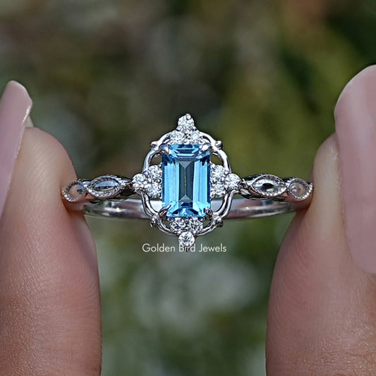 Silver halo gemstone ring with blue emerald-cut center and round accent stones