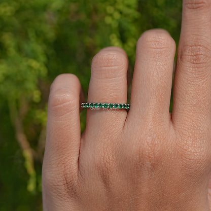 Emerald green round eternity band ring on finger, stone row across the top