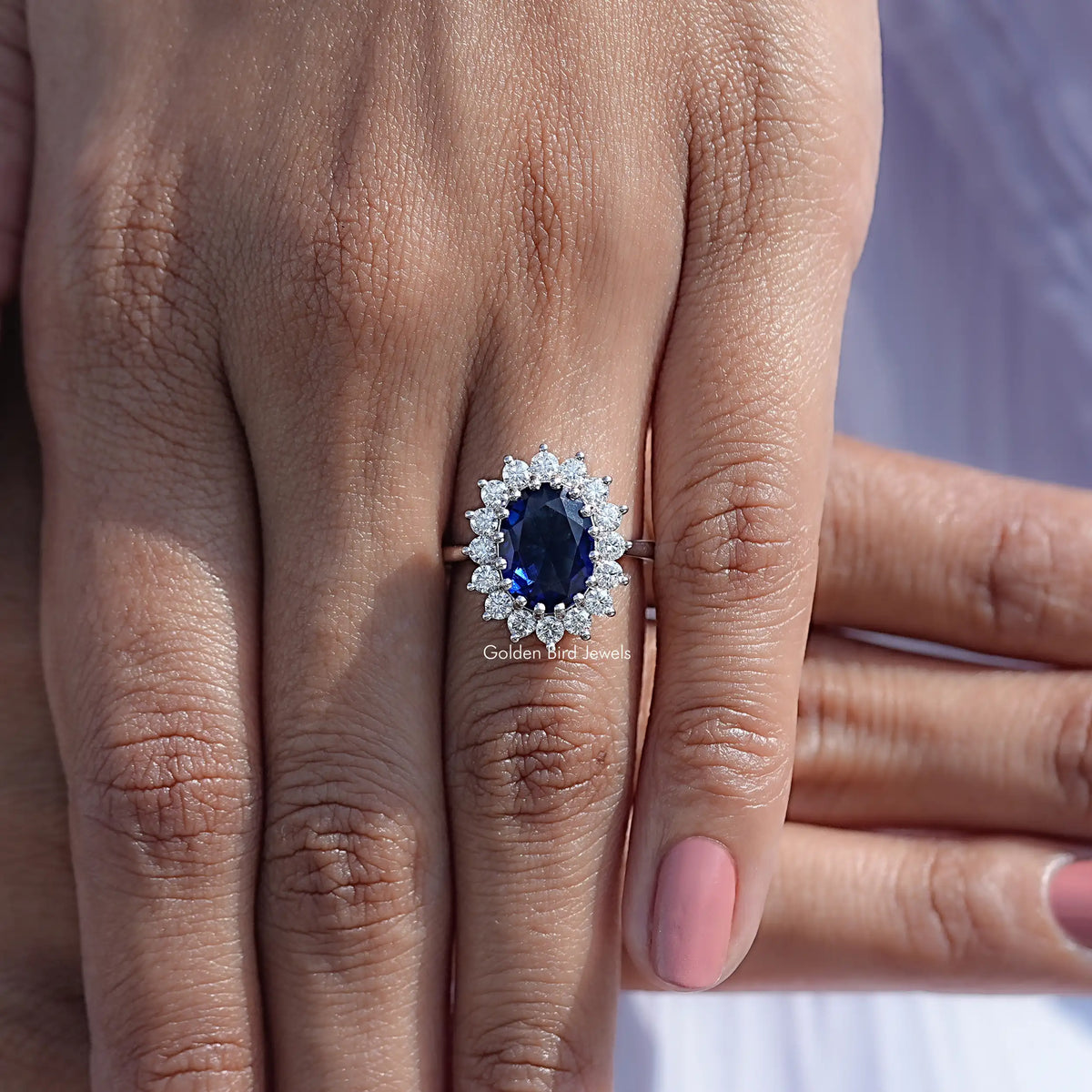 Oval blue gemstone halo engagement ring on hand, round side stones framing the center