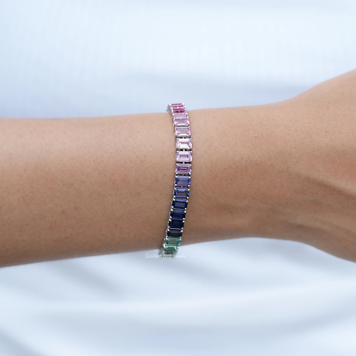 Multi-color gemstone tennis bracelet on wrist with rows of blue, green and pink stones