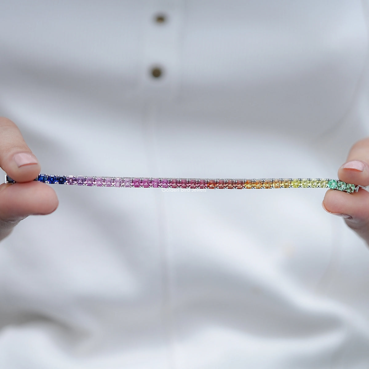 Tennis bracelet laid flat, multicolor gemstones across a silver bar setting.