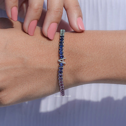 Oval gemstone tennis bracelet with small cross charm, blue to pink gradient stones