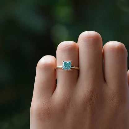 Silver princess-cut solitaire ring with cyan-blue square center stone on finger