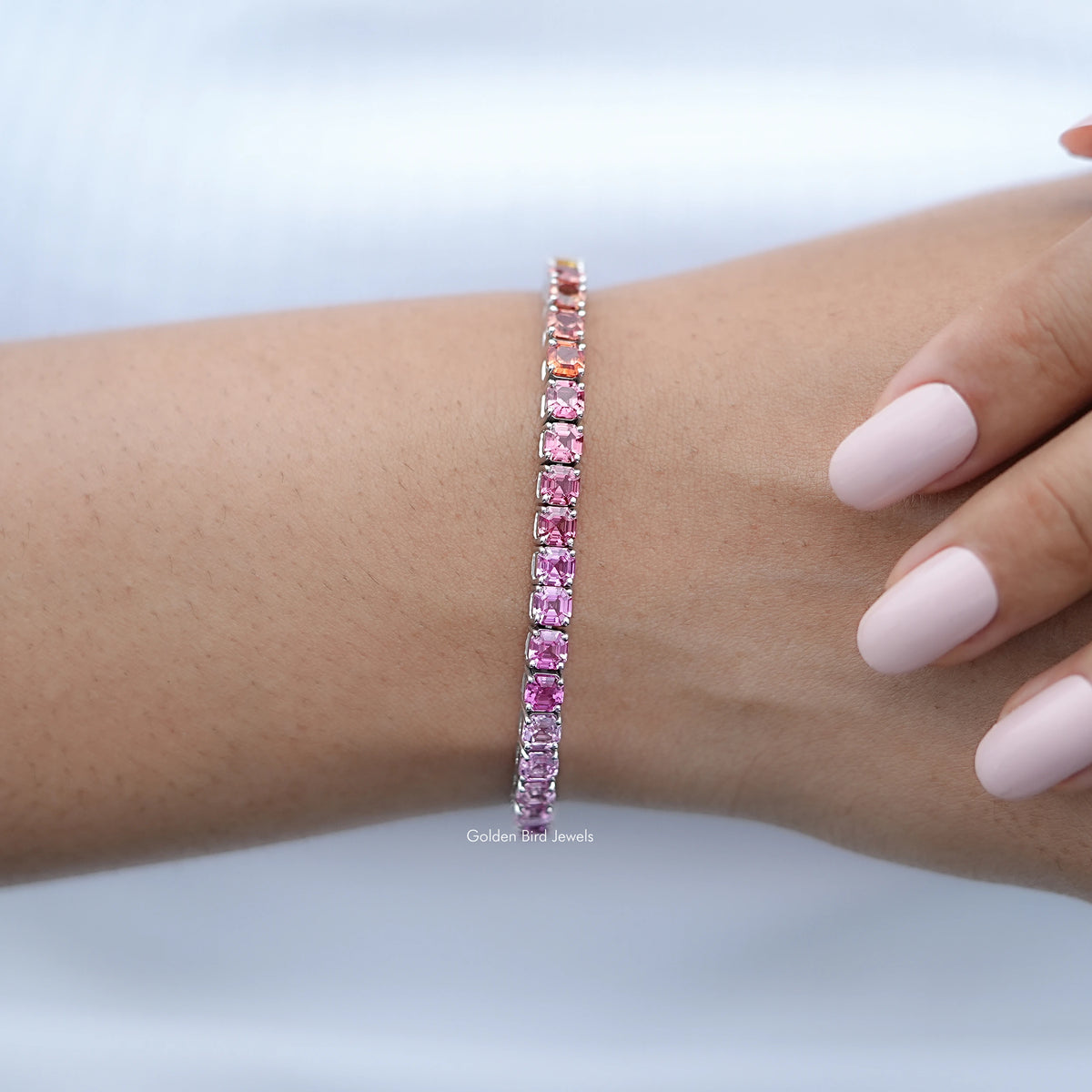 Multi-color gemstone tennis bracelet on wrist, pink to purple gradient stones in silver prongs.