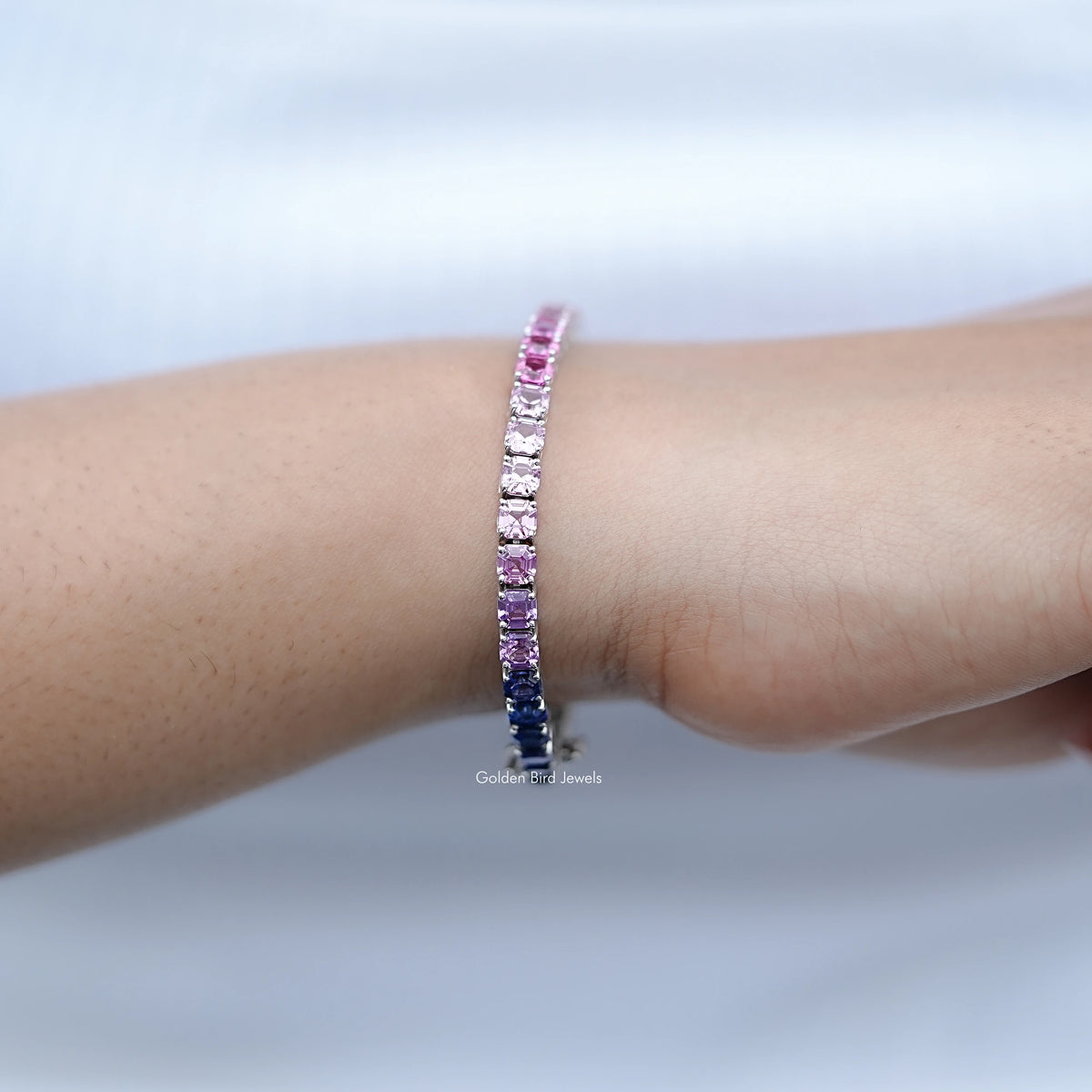 Gradient tennis bracelet on wrist, pink stones with dark blue sections in silver setting.