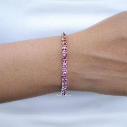 Gradient gemstone tennis bracelet on wrist, pink and orange-hued stones in silver prongs.