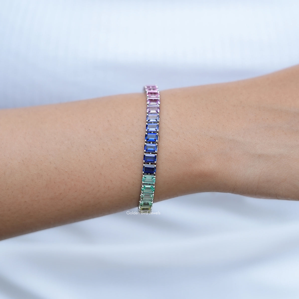Multi-color gemstone tennis bracelet on wrist with pink top row and blue-green accents