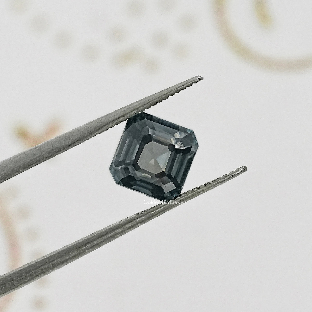 Gray Asscher-cut moissanite gemstone close-up held by tweezers