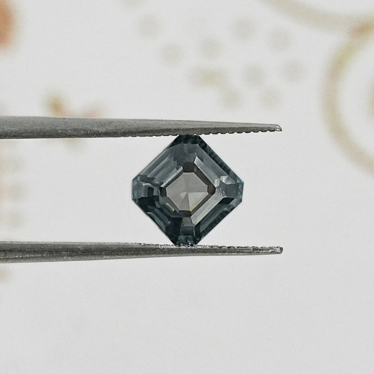 Gray Asscher-cut moissanite gemstone held between two metal tweezers