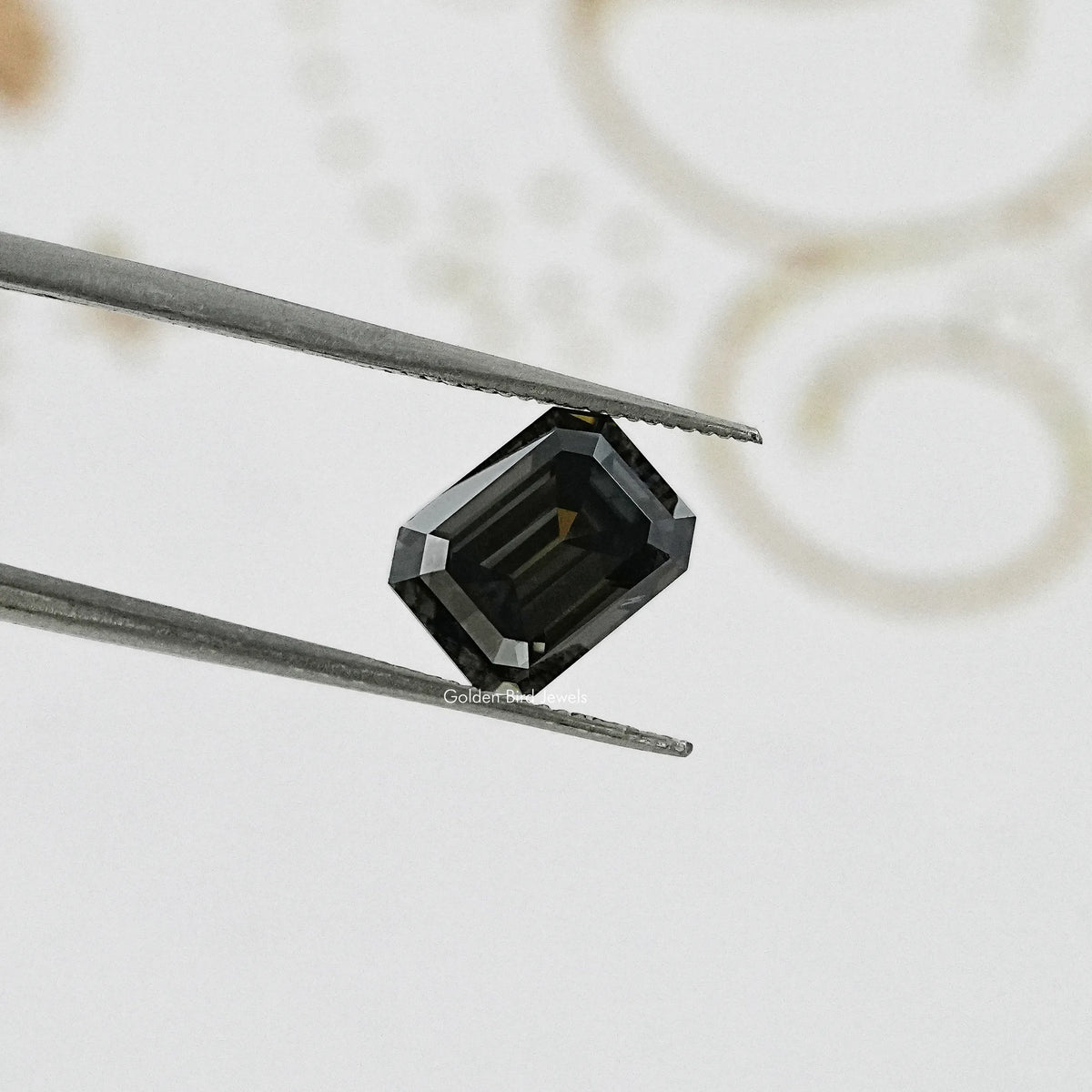 Dark gray emerald-cut moissanite gemstone pinched by tweezers