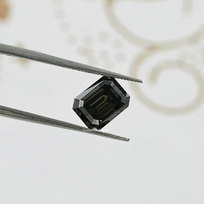 Dark gray emerald-cut moissanite gemstone pinched by tweezers