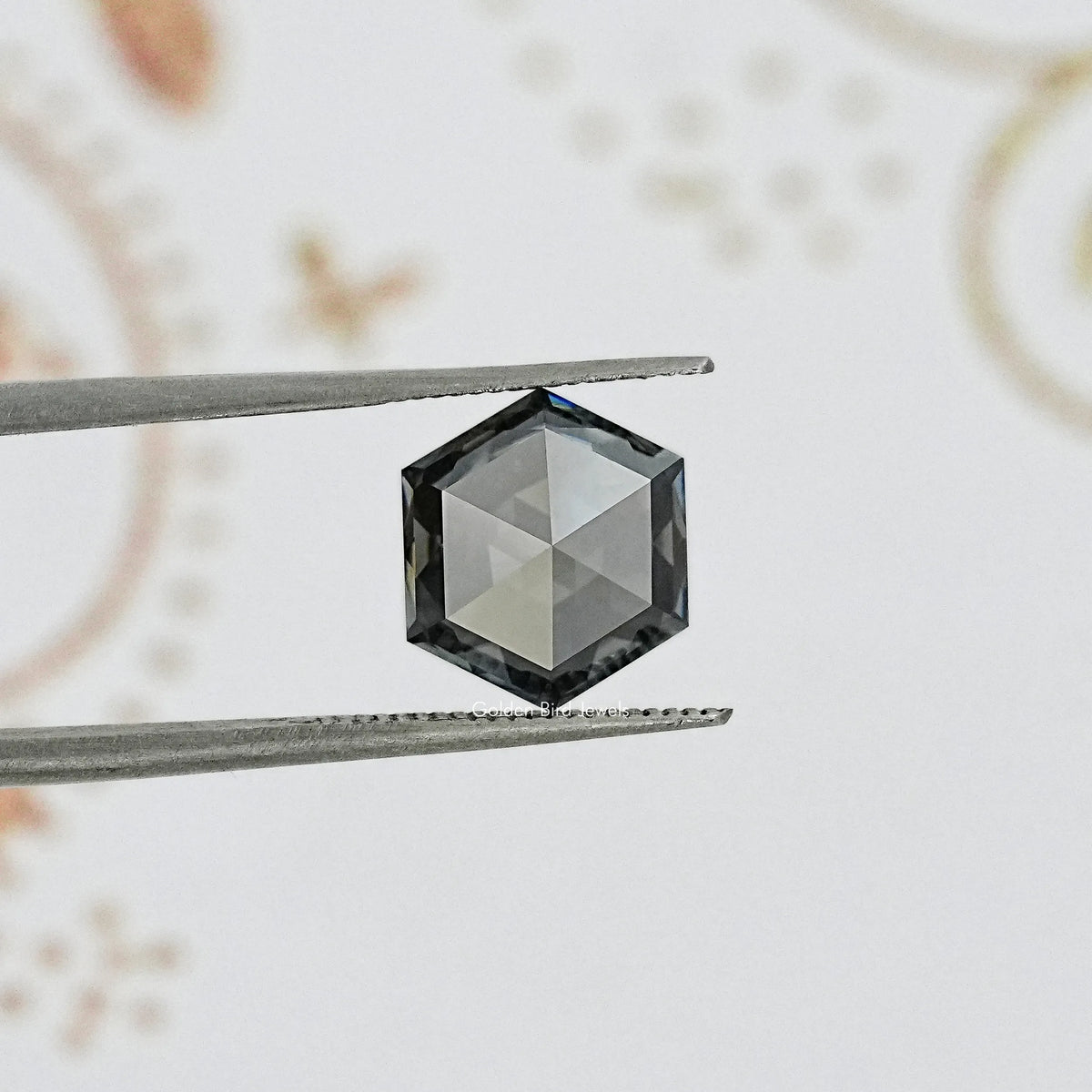 Hexagon-cut gray moissanite gemstone held between tweezers, faceted dark tone