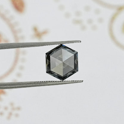 Hexagon-cut gray moissanite gemstone held between tweezers, faceted dark tone