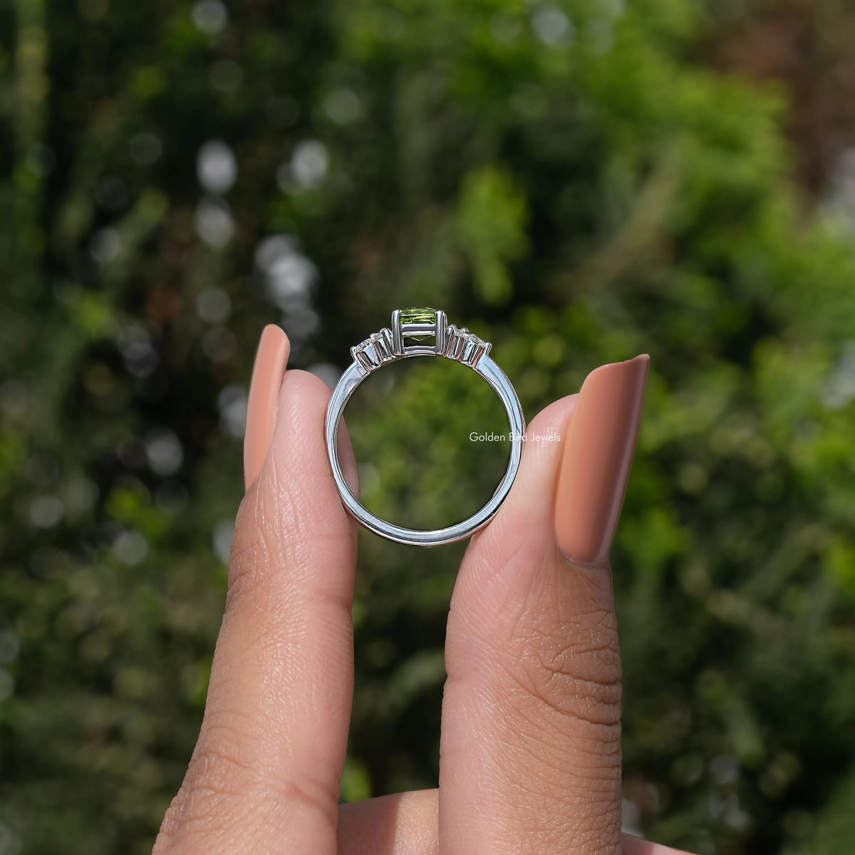 Silver ring with emerald-cut green center stone and halo, viewed from behind