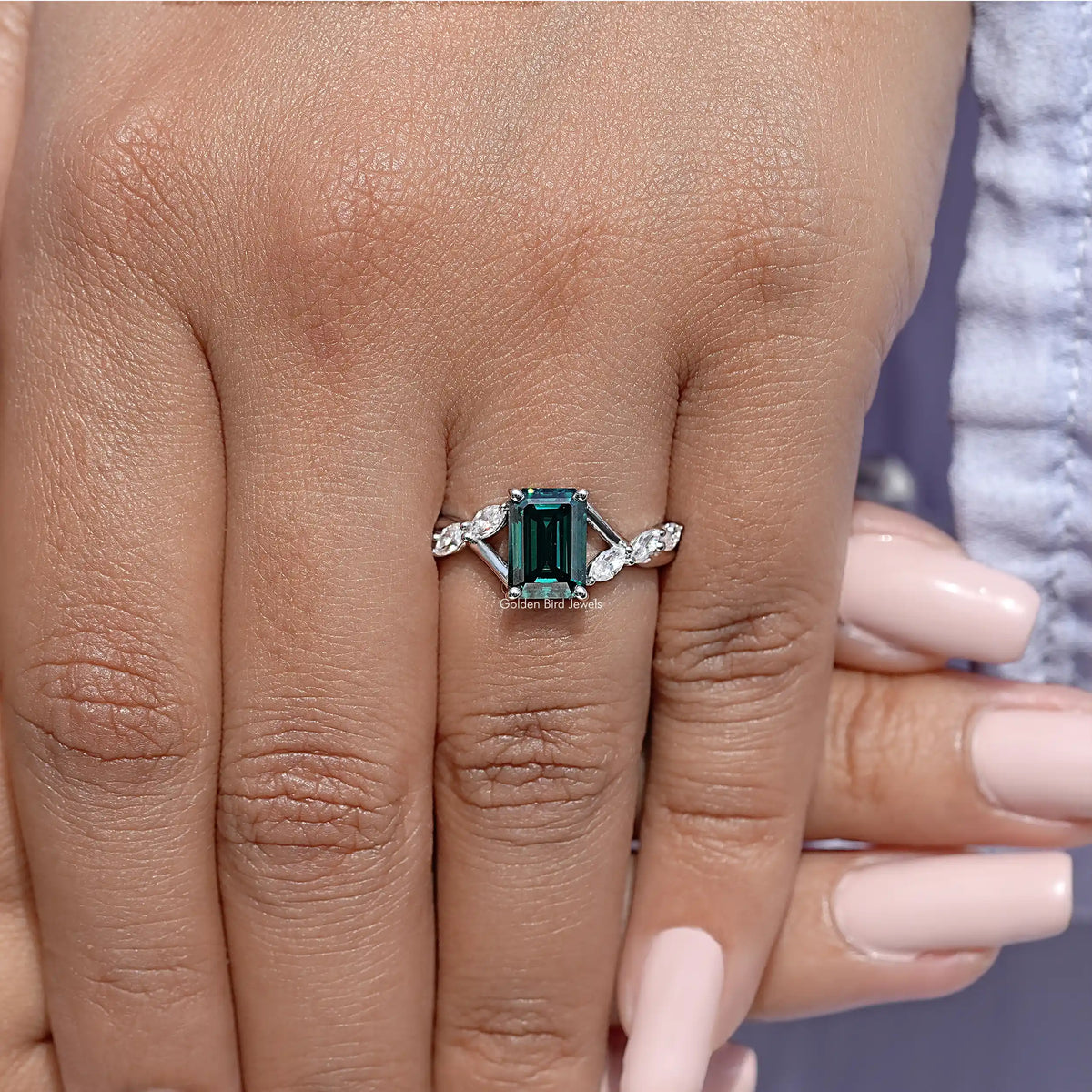 Sterling silver green emerald-cut moissanite ring with floral shoulders on hand.
