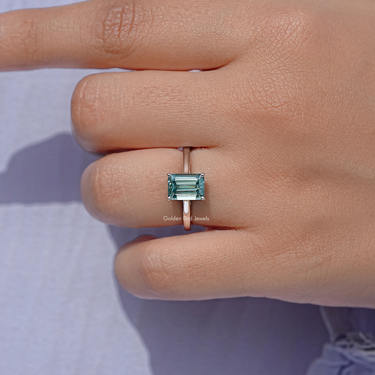 Emerald-cut moissanite solitaire ring, teal stone set in silver prongs
