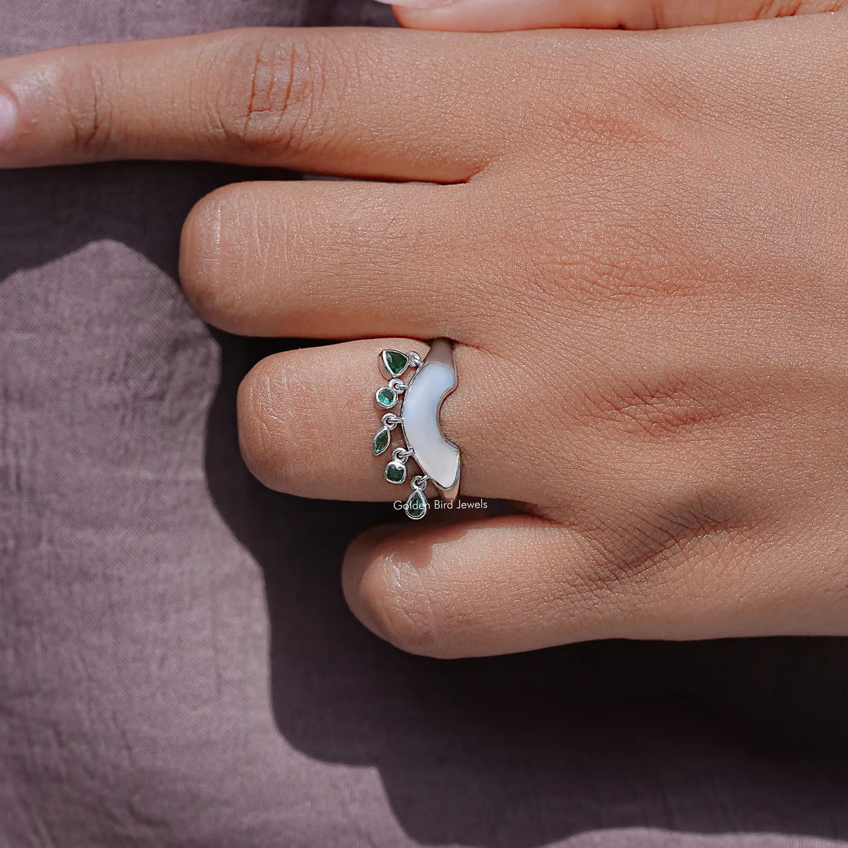 Curved bezel-set engagement ring with green gemstones on tapered silver band