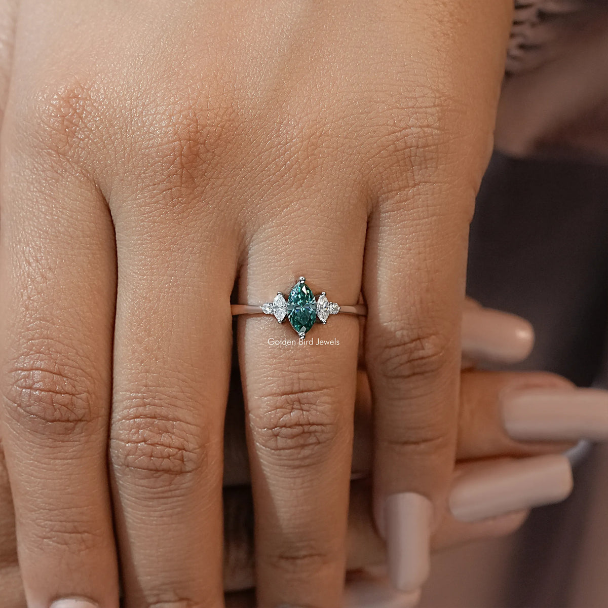 Three-stone engagement ring on hand, green marquise center with two marquise side stones