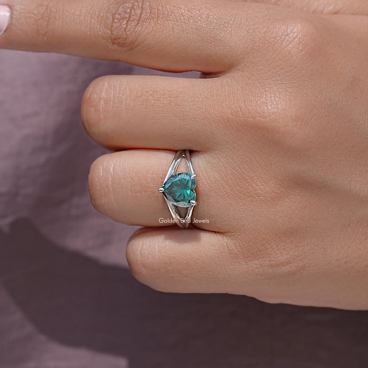 Sterling silver heart-cut teal moissanite ring, split shank, close-up on fingertip