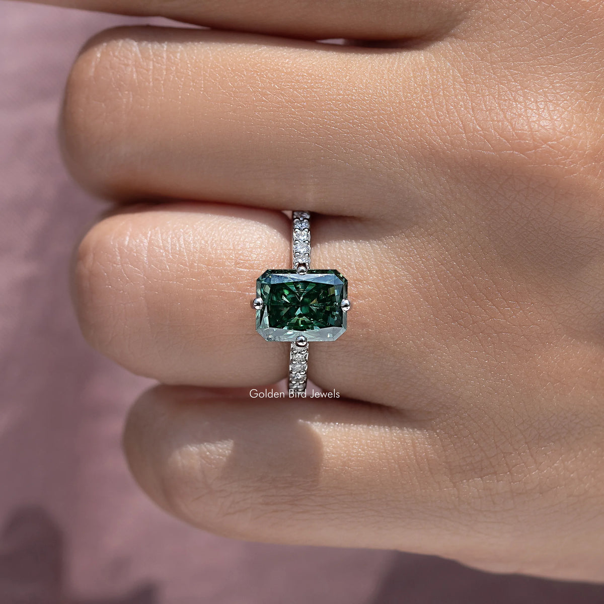 Emerald-cut moissanite solitaire ring with dark green center stone and side diamond accents