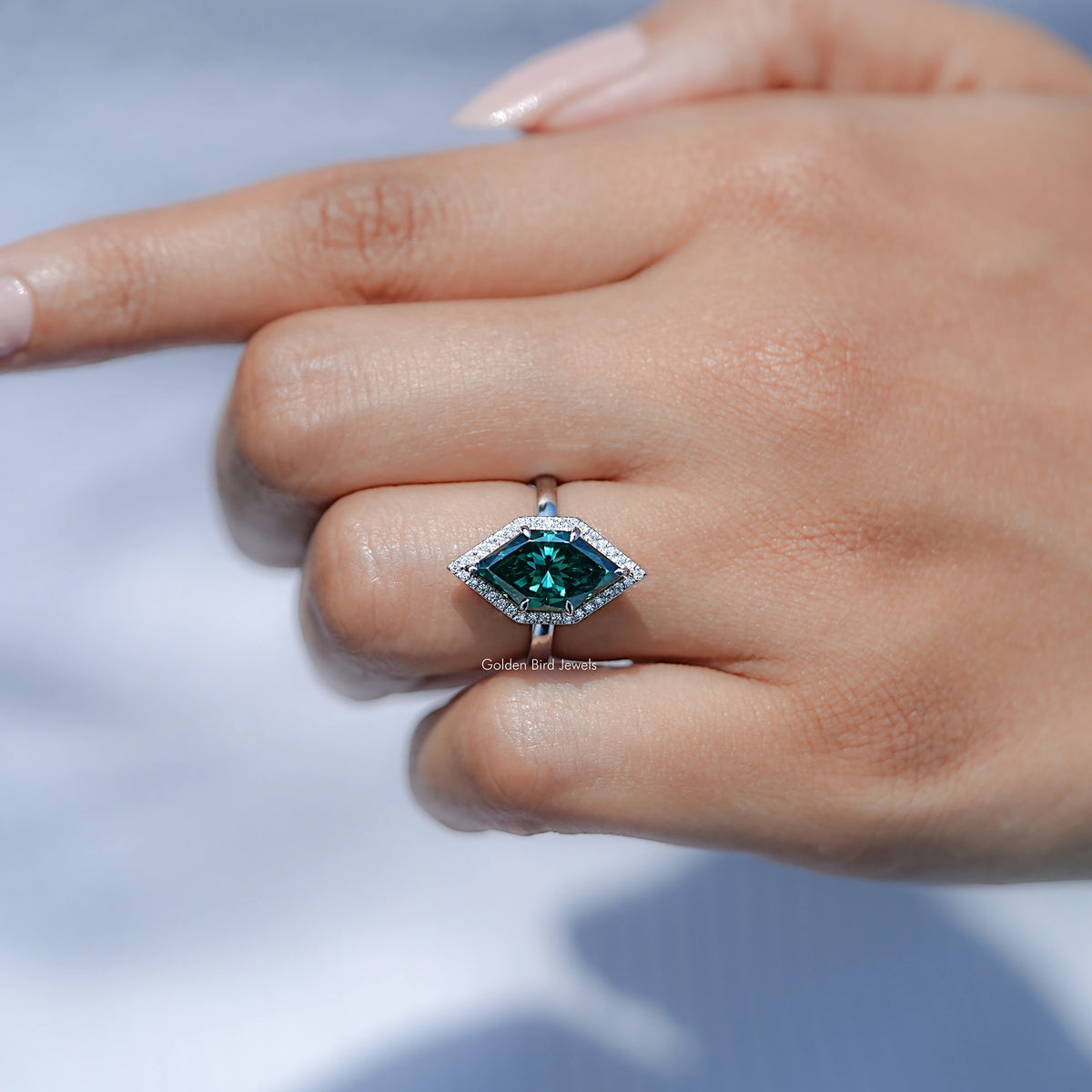 Teal marquise halo engagement ring with rectangular center stone, ring on resting hand