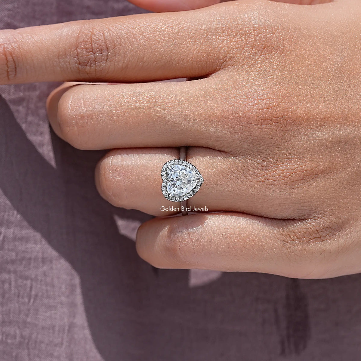 Heart-cut moissanite halo ring close-up on knuckle, heart center with halo stones
