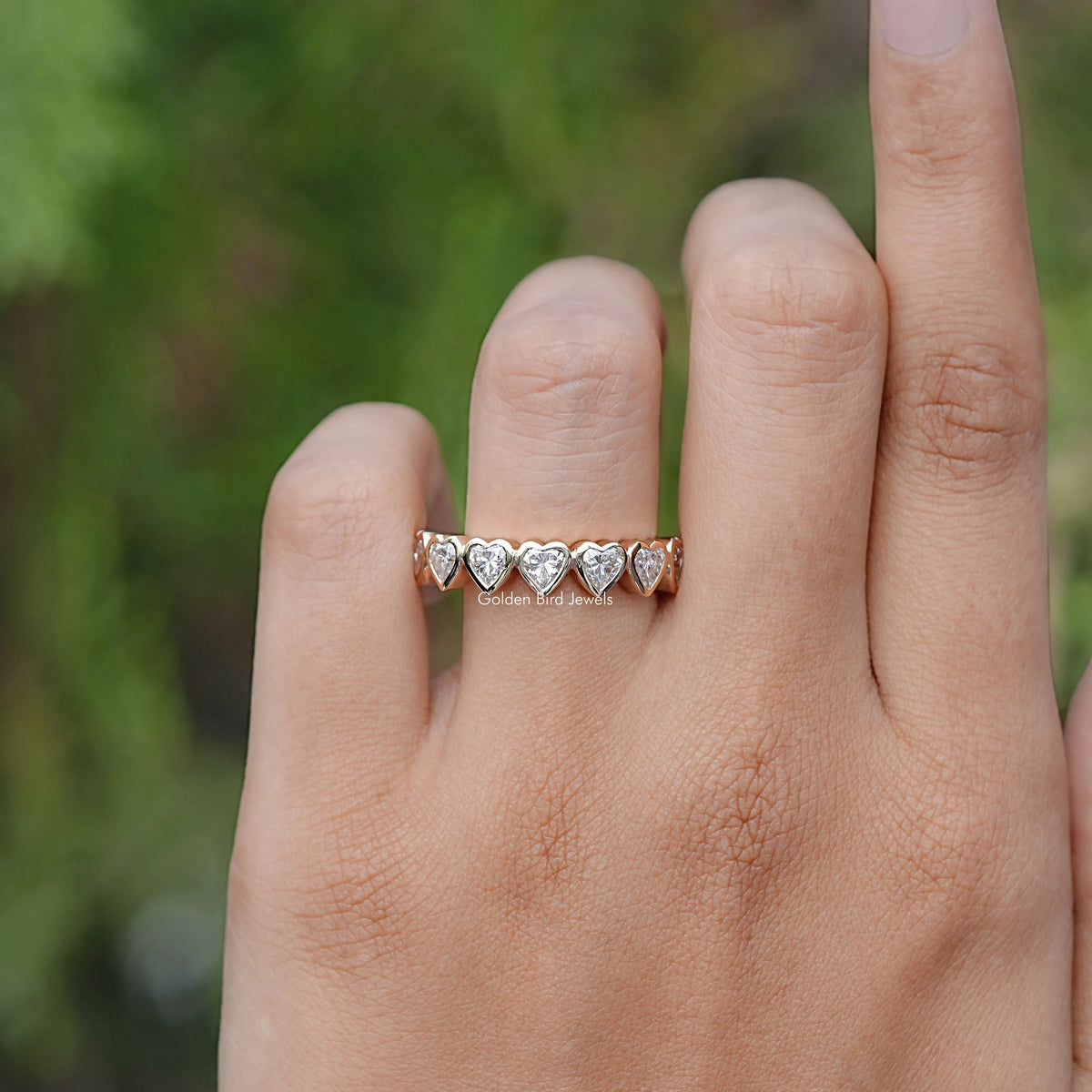 Heart-shaped eternity band ring with bezel-set stones, worn on a finger