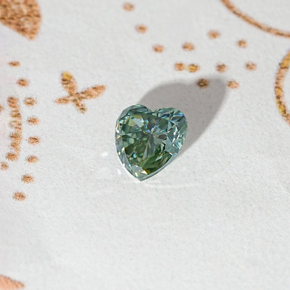 Heart-cut moissanite gemstone, light green-blue with faceted crown and shine.
