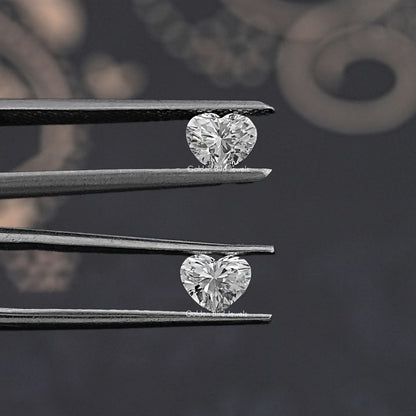 Heart-cut loose diamonds held by tweezers, two matching stones