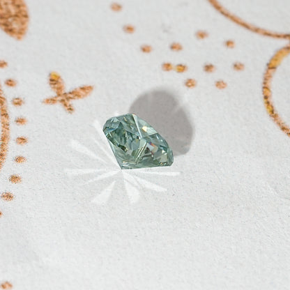 Heart-cut moissanite gemstone, green-blue with multi-facet pattern and sparkle.