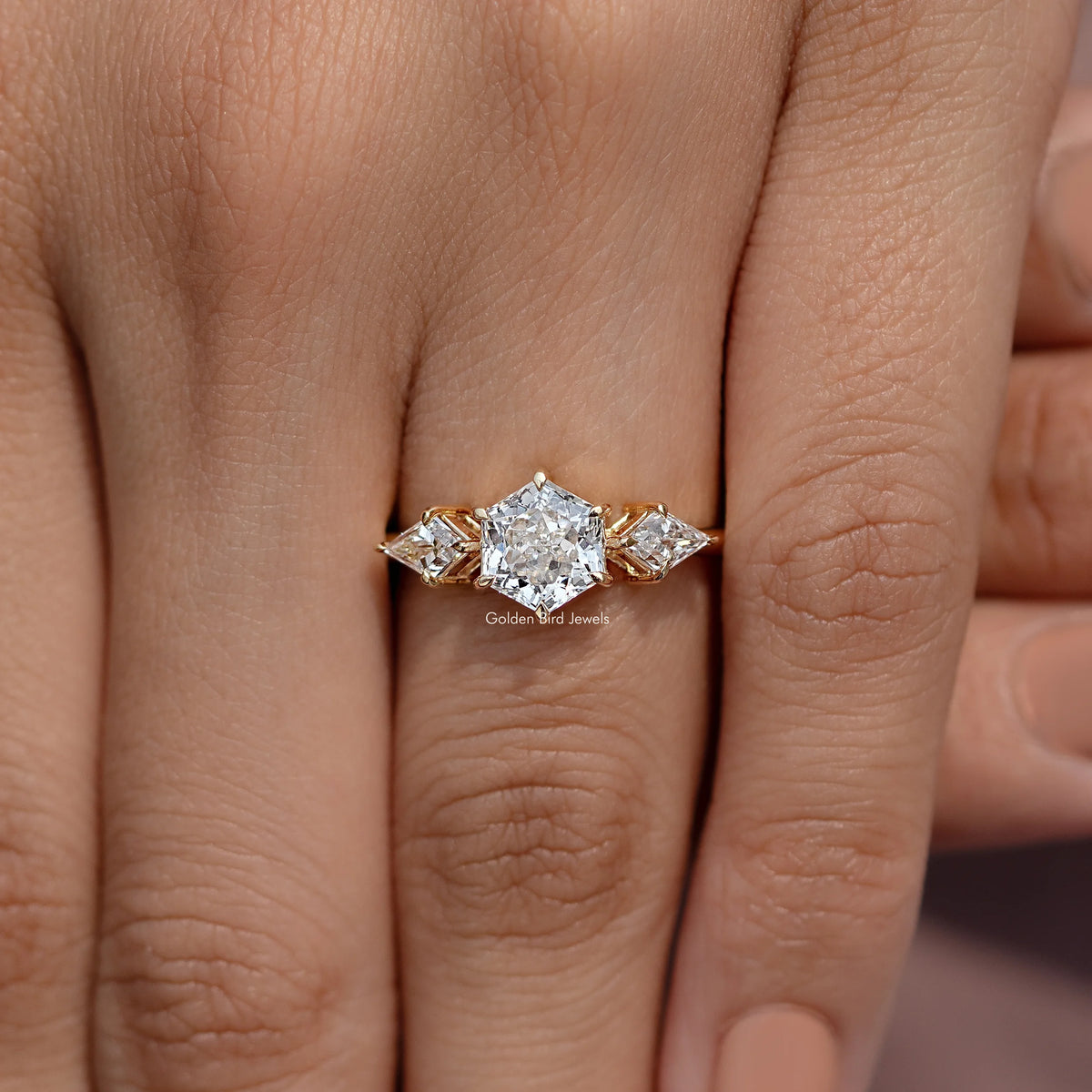 Three-stone diamond ring on fingers with faceted center stone and two side stones, gold