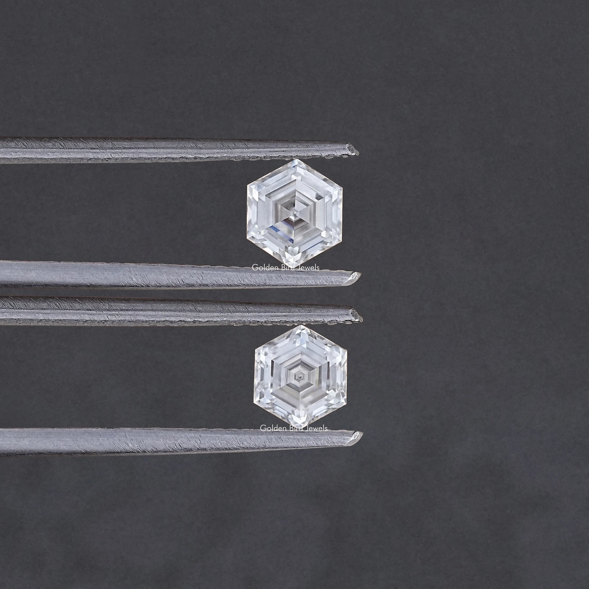 Faceted hexagon-cut moissanite pair held between metal tweezers