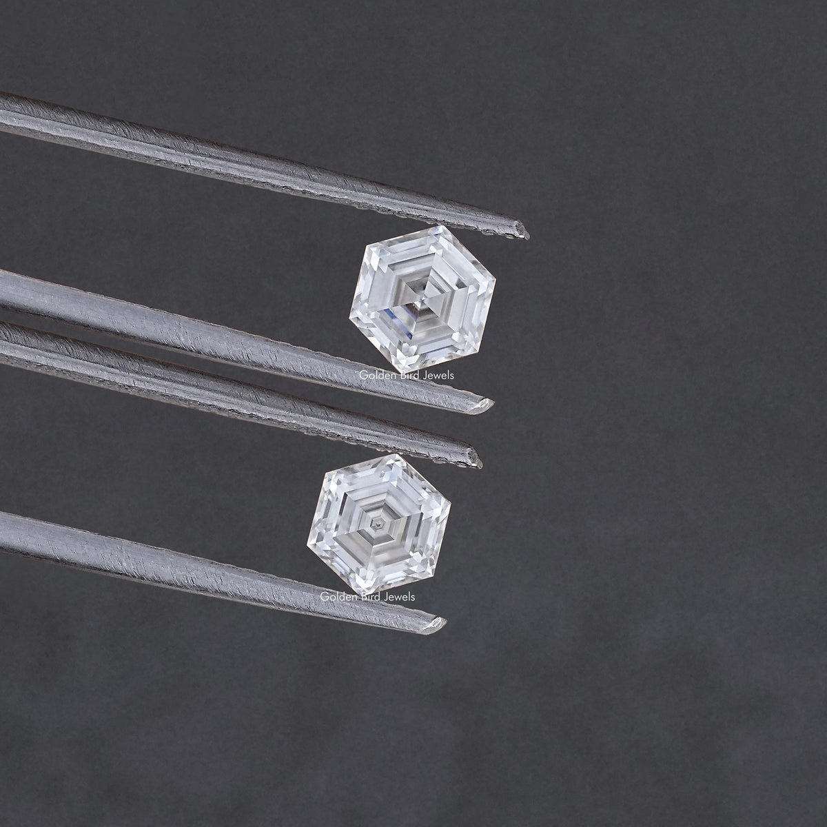 Faceted hexagon-cut moissanite pair held between metal tweezers