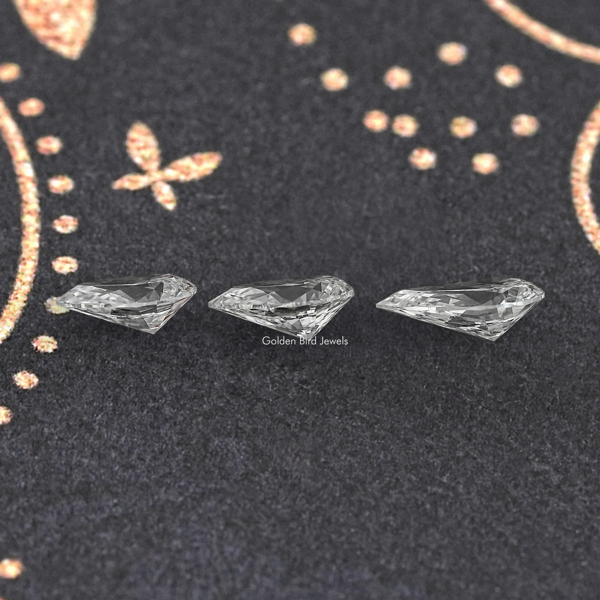 Loose pear-cut lab diamond, three stones displayed on dark fabric