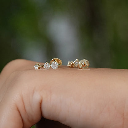 Gold-tone three-round-stone stud earrings, reverse side on fingertip