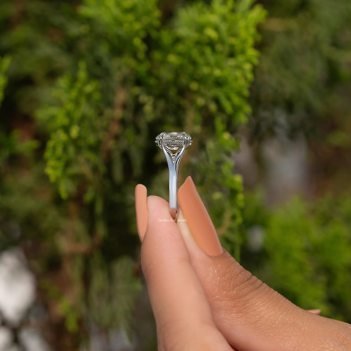 Cushion-cut diamond split-shank ring held between fingers, profile view