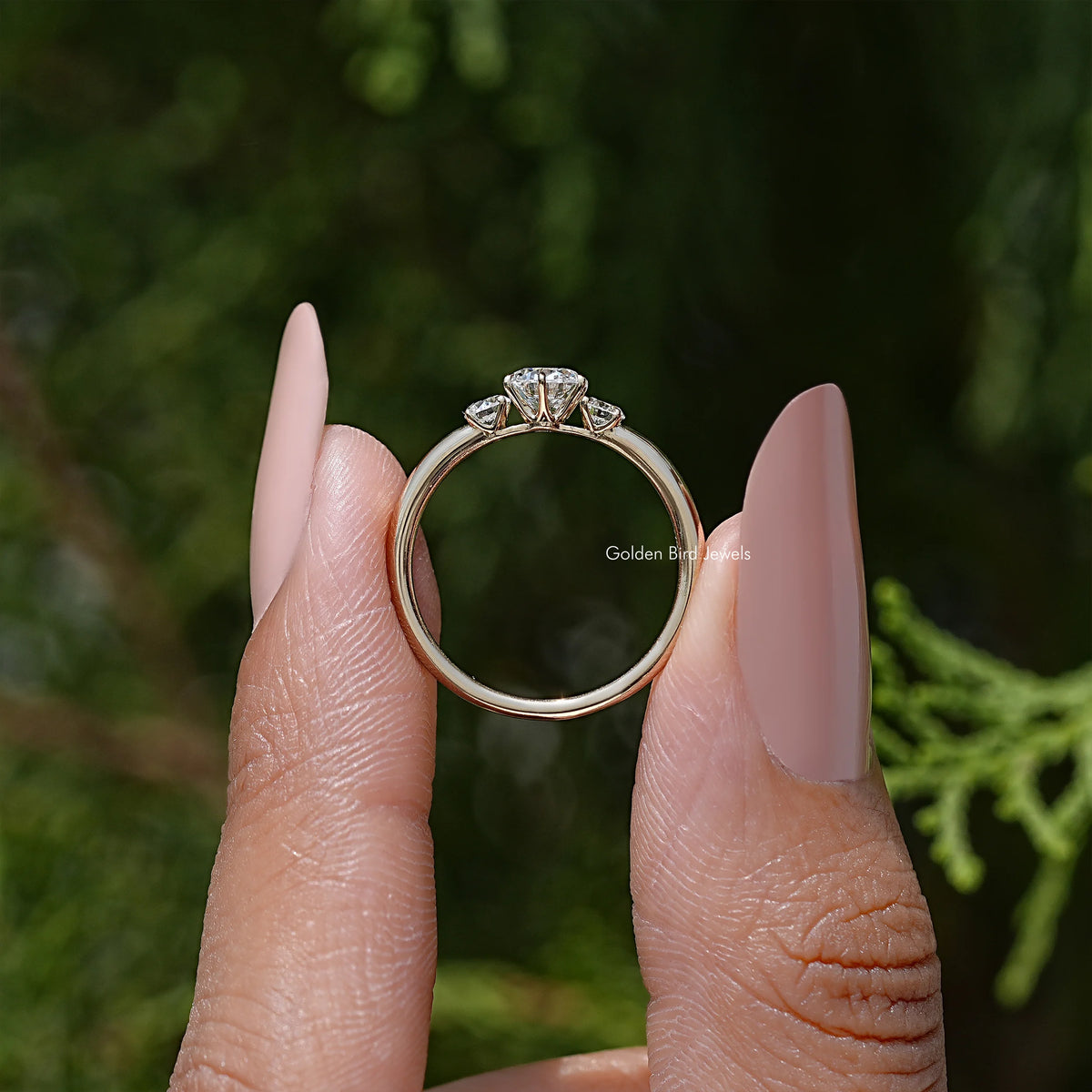 Three-stone round diamond ring viewed from side, slim band with prong-set center stone