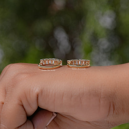 Gold-tone emerald-cut lab diamond hoop and huggie earrings shown on fingertip close-up