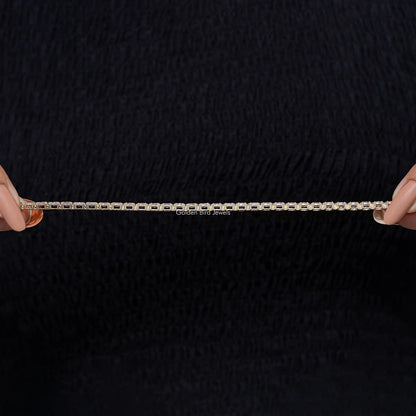 Gold-tone tennis bracelet with marquise-cut lab-grown diamonds, held between fingers