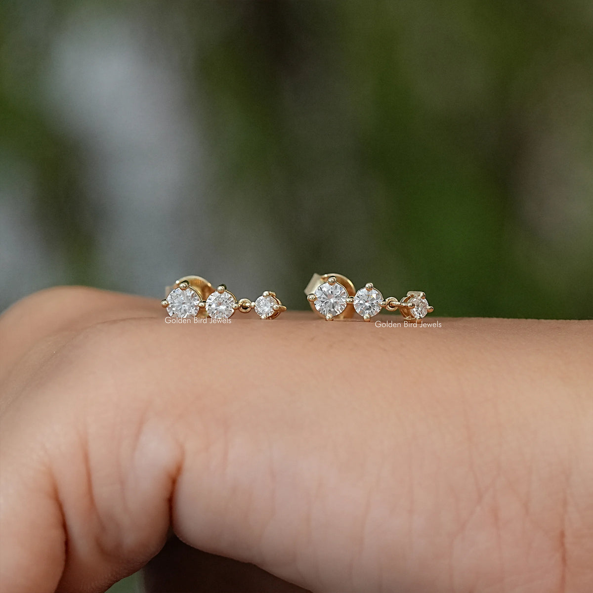 Gold-tone trio of round-stone stud earrings, side view on fingertip