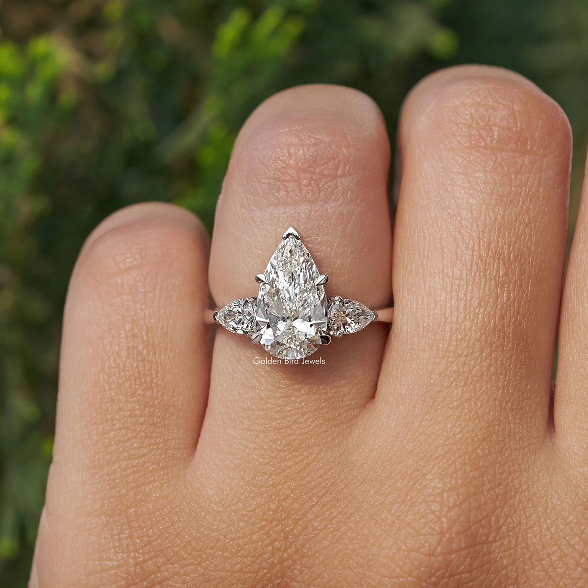 Three-stone pear-cut diamond engagement ring on fingers, center pear with side stones