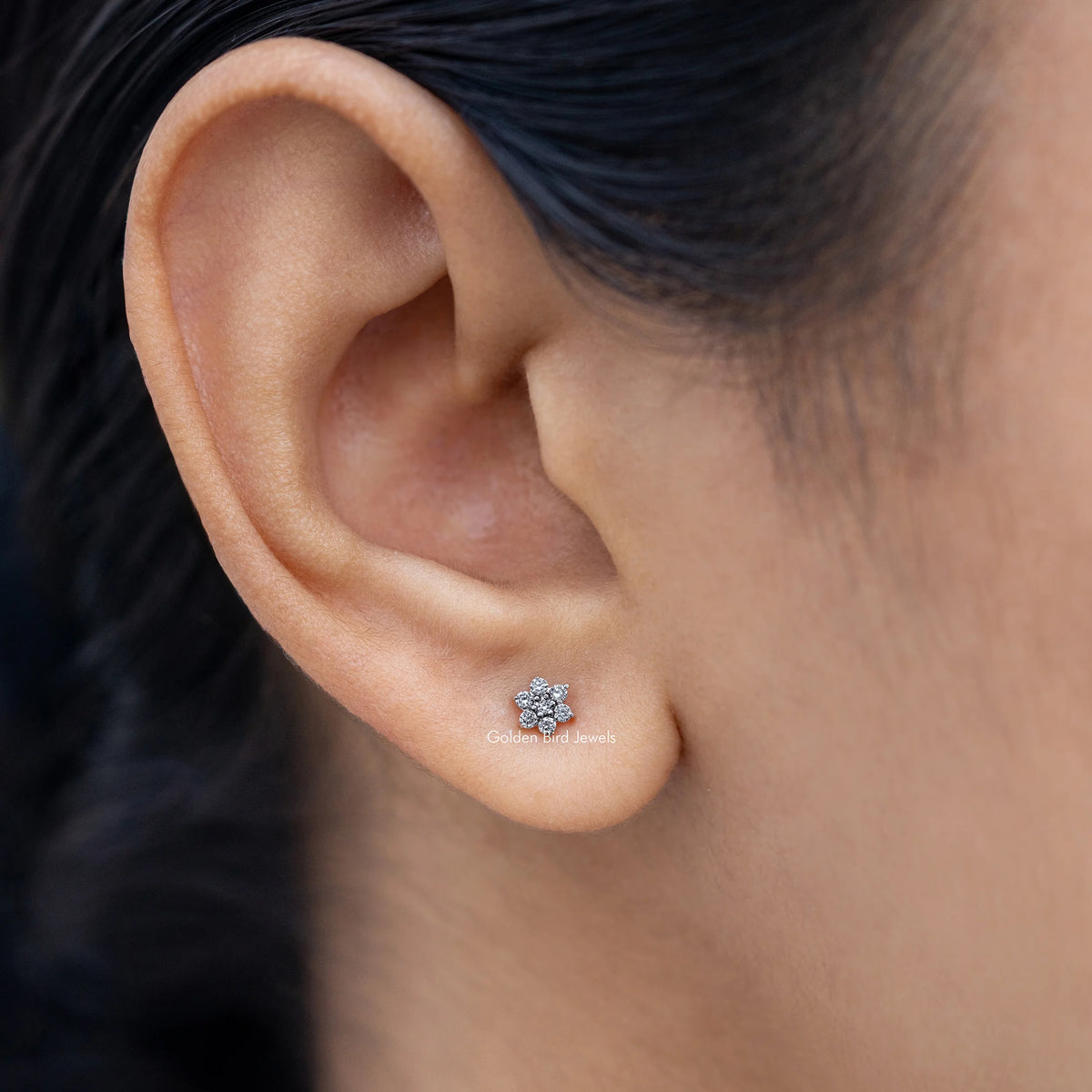 Floral diamond stud earring on ear, small round flower-like stone cluster.
