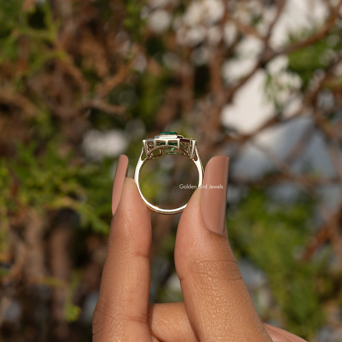 Gold-tone ring from side/back with emerald-green center stone and clear halo