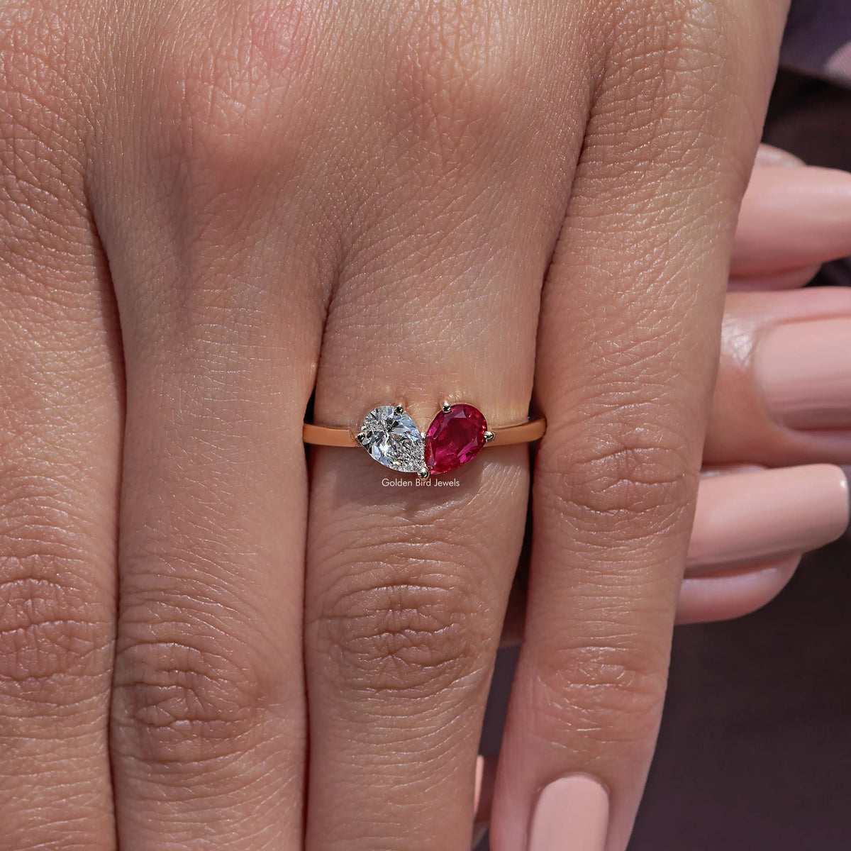 Gold-tone ring with a round diamond and red pear-cut gemstone on a slim band