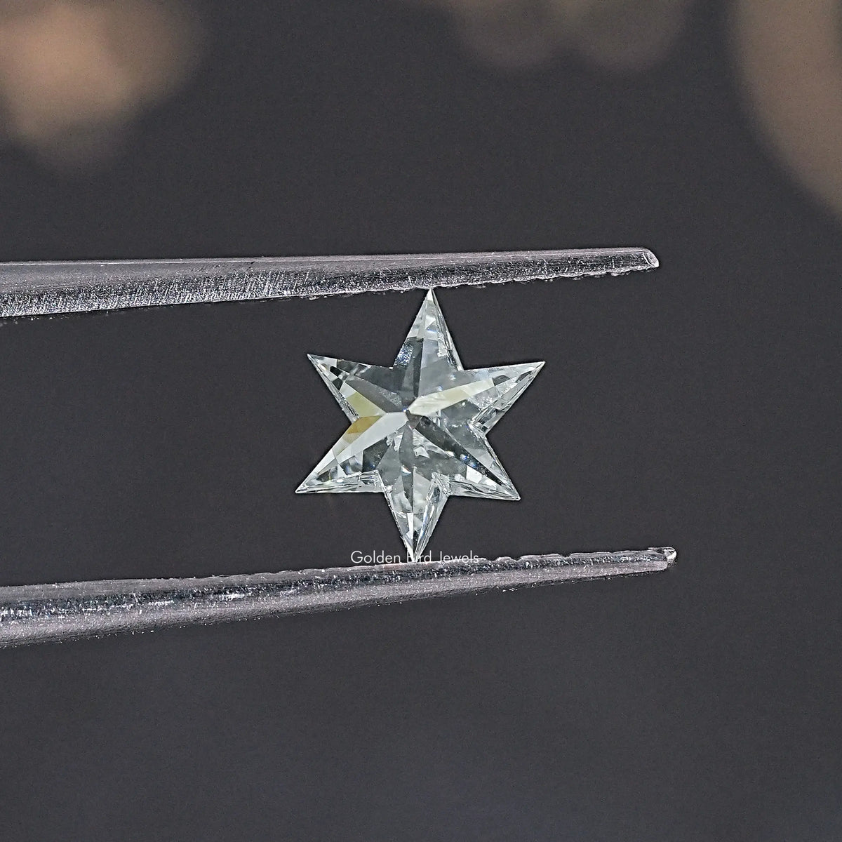 Star-cut loose lab-grown diamond in tweezers, faceted star front view