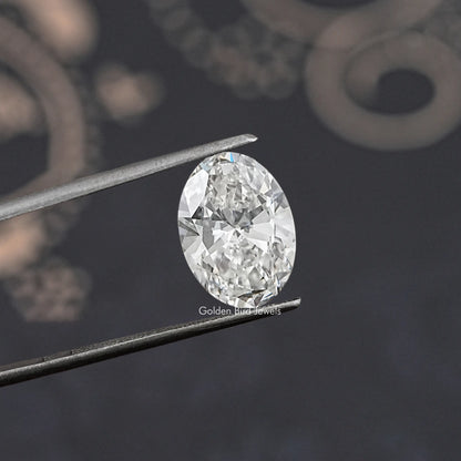 Oval-cut lab-grown diamond on tweezers, angled view of faceted surface