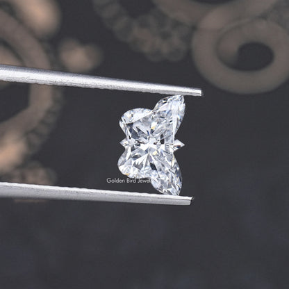 Butterfly-cut lab-grown diamond in tweezers, side view of bright facets