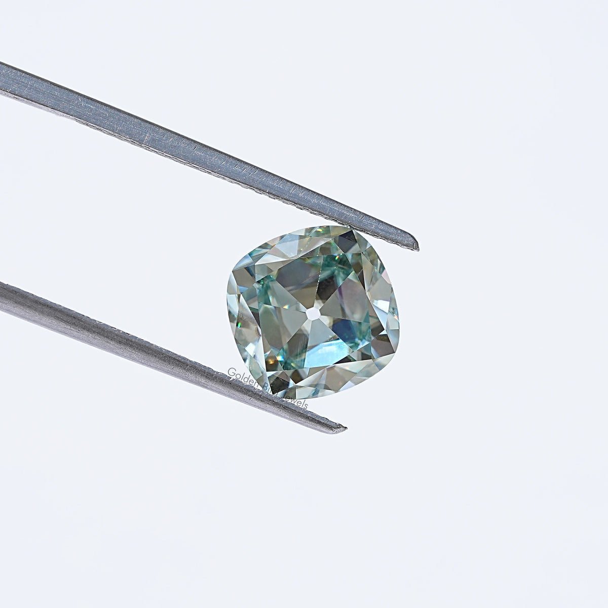 Light blue moissanite gemstone in silver tweezers, cushion old mine cut