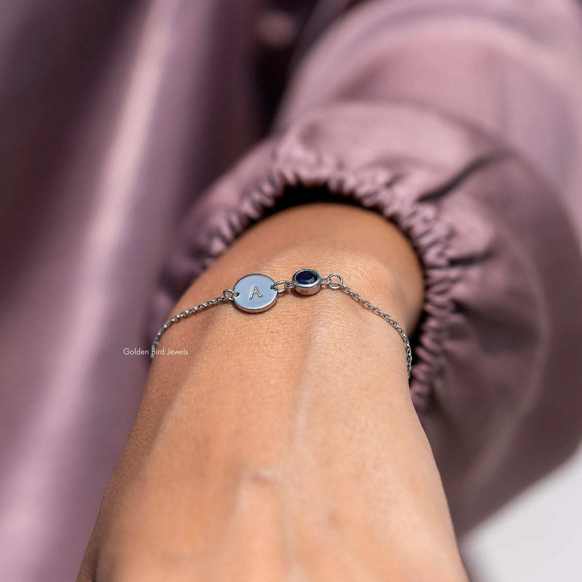 Bracelet wrist shot with round light blue initial A charm and dark blue gemstone center